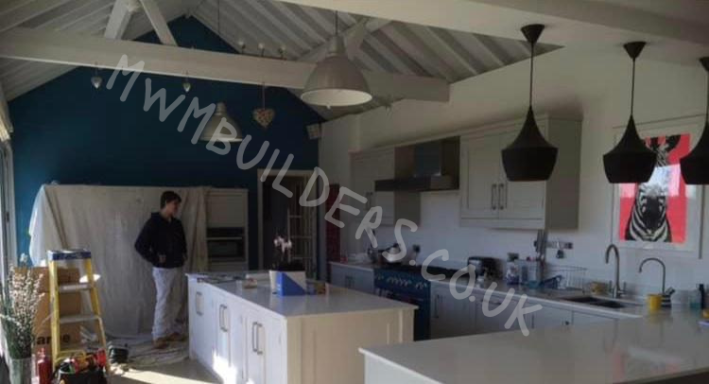 Modern kitchen with white cabinets, blue accent wall, and pendant lights; a person is present.