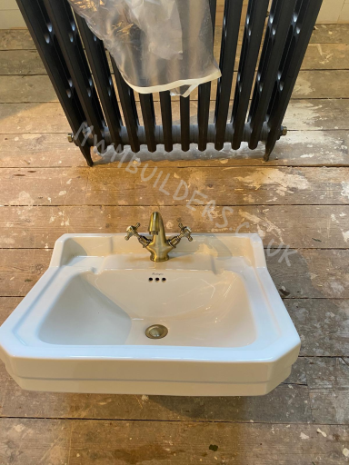 White sink with a gold tap, set on a wooden floor near a black radiator.