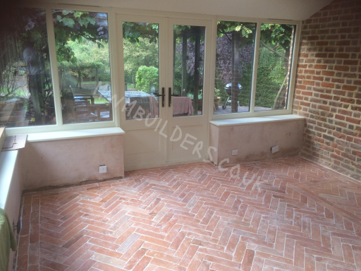 Interior of a sunroom with herringbone patterned flooring and large windows.