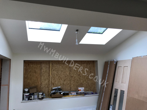 Bright room with two skylights, featuring a boarded window and construction materials.
