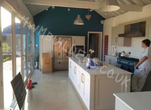 Modern kitchen with a blue accent wall, large windows, and a person standing by the counter.