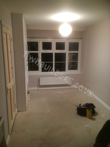 Empty room with pale walls, large window, and a light fixture overhead. Tools are on the floor.