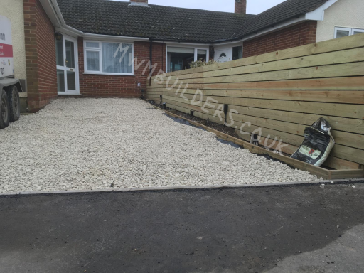 Gravel driveway with wooden fencing alongside a bungalow.