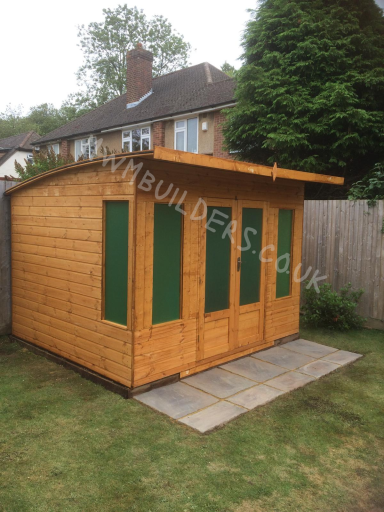 Wooden garden shed with green doors and a sloped roof, set on a stone patio.