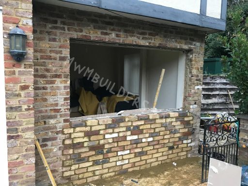 Construction area showing a partially bricked-up window with tools and materials nearby.