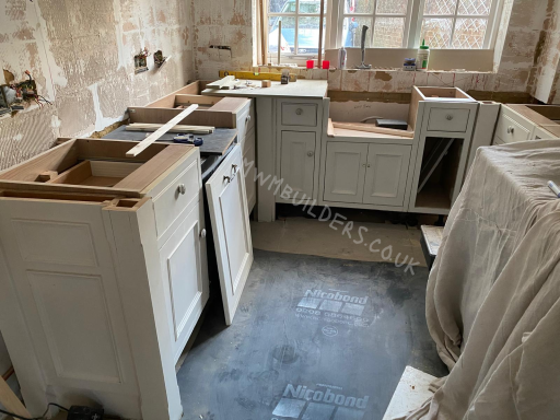 Unfinished kitchen with white cabinets and exposed plumbing in a renovation stage.