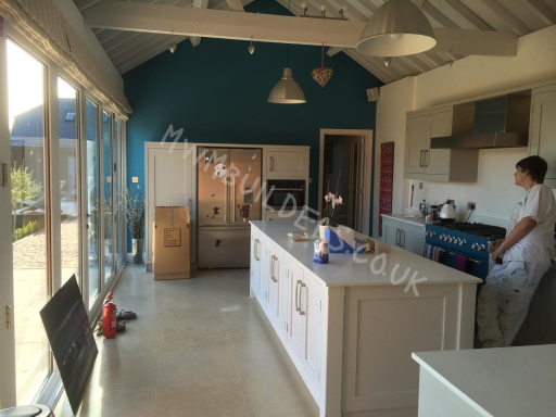 Modern kitchen with a central island, blue accent wall, and large windows.