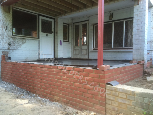 A partially completed brick wall surrounding an unfinished porch area of a house.
