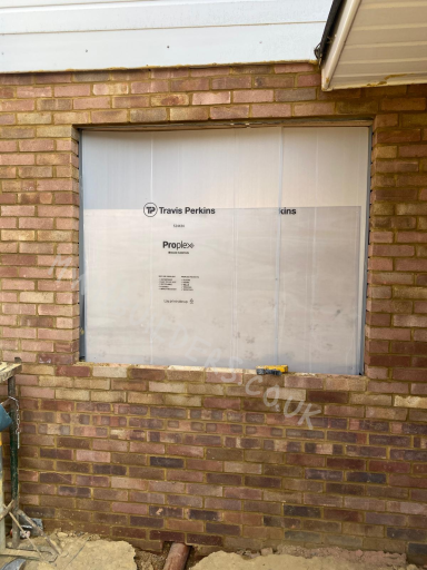 A boarded-up window with a grey metal panel on a brick wall.