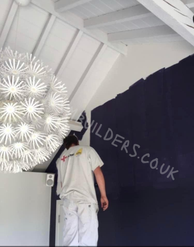 A person painting a dark wall under a decorative white light fixture.
