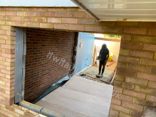 A person walking through a gap in a brick wall, with wooden planks on the ground.