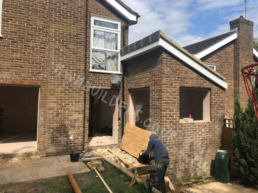 Renovation work on a brick house with open windows and construction materials outside.