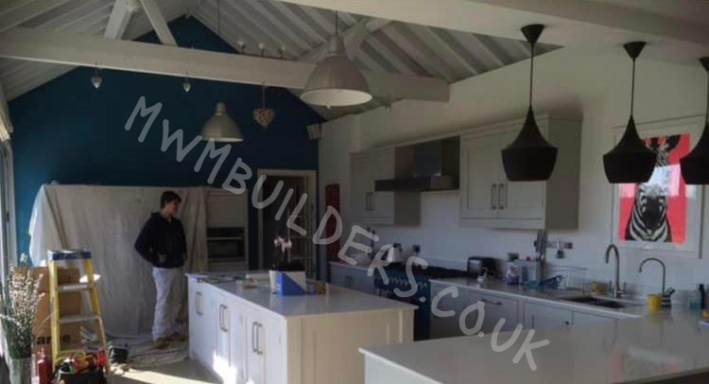 Modern kitchen with blue accent wall, pendant lights, and a person standing by the counter.